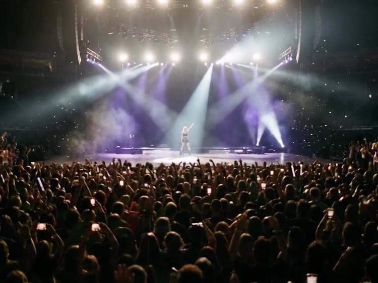 AI-generated still from the reel: a packed arena under stage lights, a singer on a distant stage.