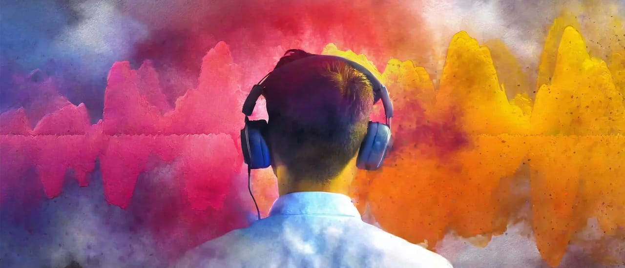 A person in headphones seen from behind, surrounded by clouds of bright pink, orange and blue colour.