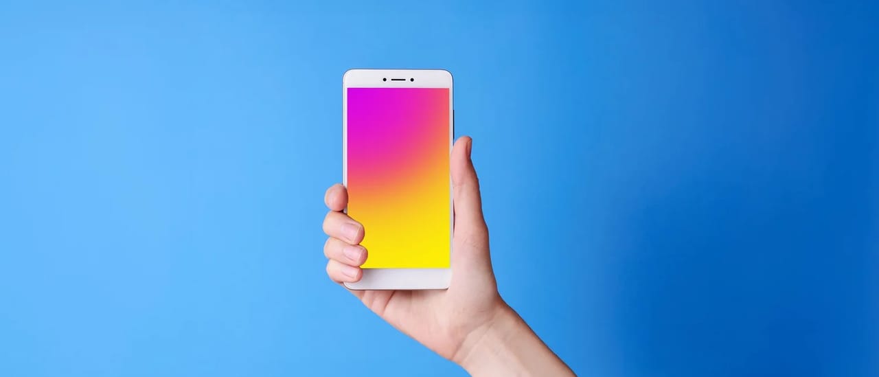 A hand holding a smartphone upright, its screen glowing pink, against a plain blue background.