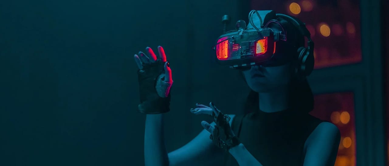 A person in a virtual-reality headset reaching out with gloved hands in a dim teal room.