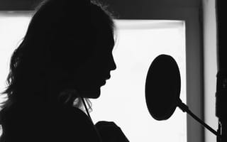 Silhouette of a voice artist speaking into a studio microphone with a pop filter.