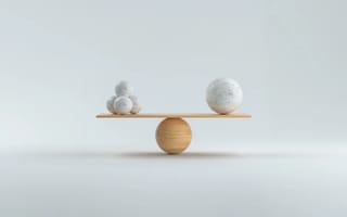 Two spheres balanced on a simple seesaw on a pale grey background.