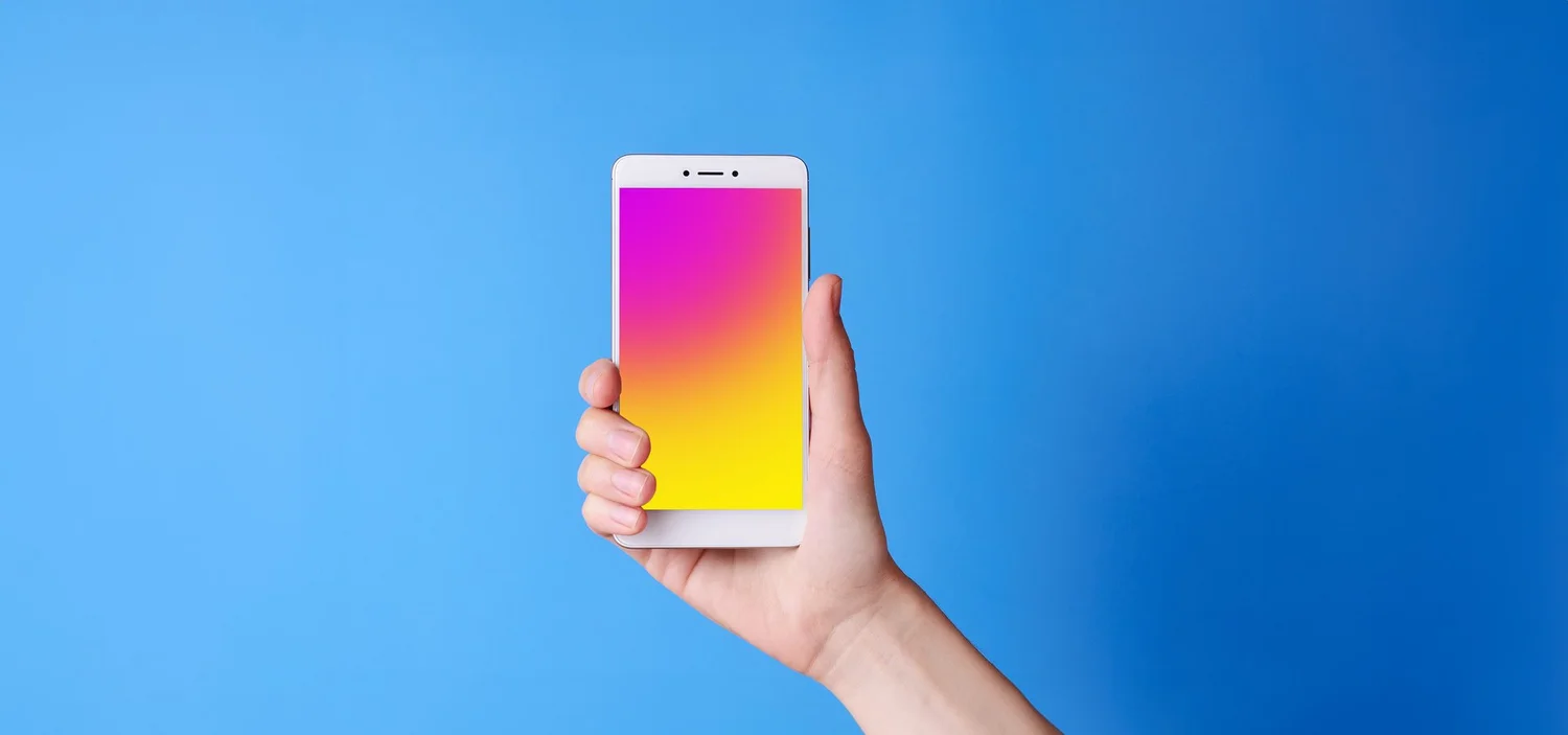 A hand holding a smartphone upright, its screen a pink-to-yellow gradient, against a blue background.